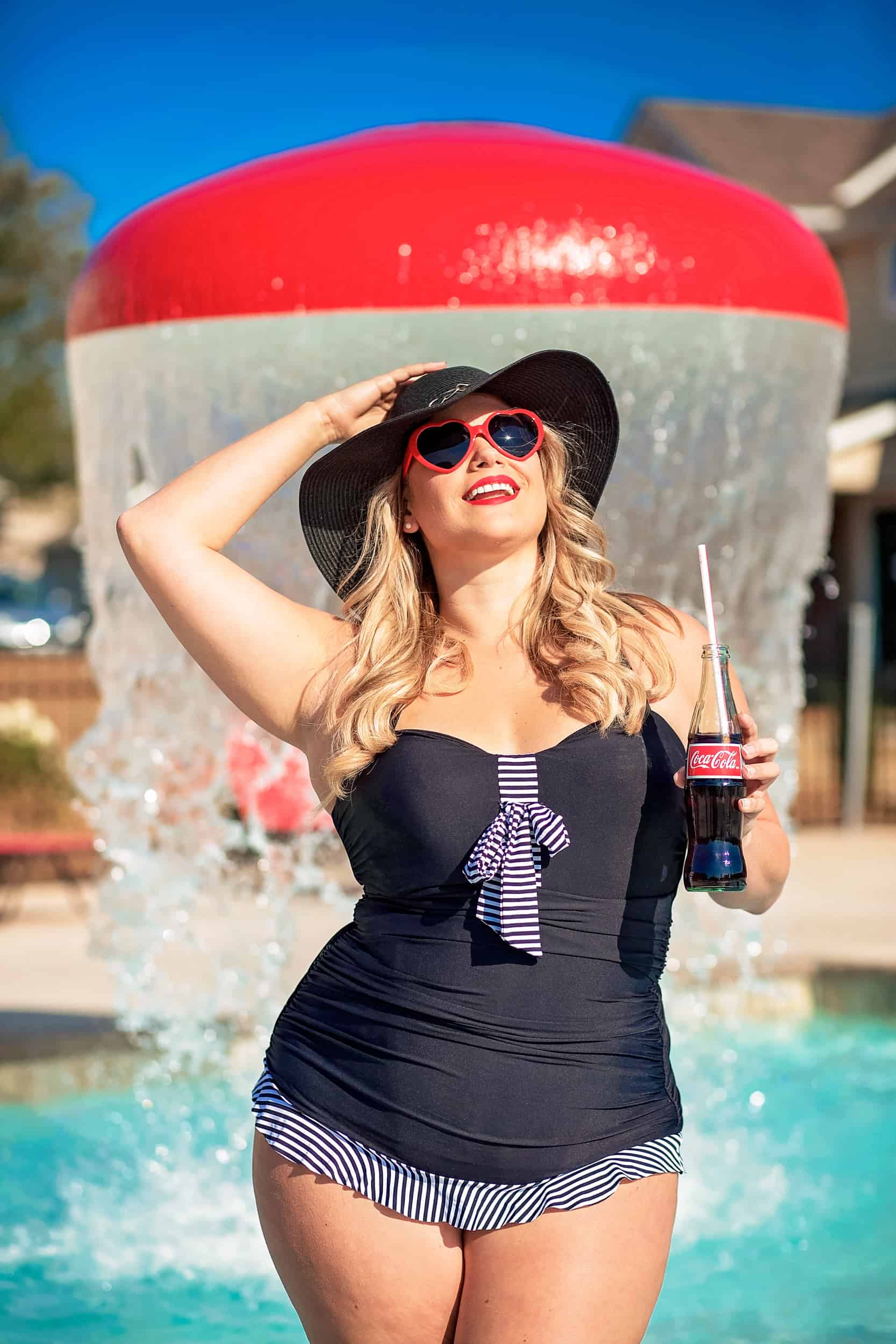 A woman in a black swimsuit standing next to a fountain.