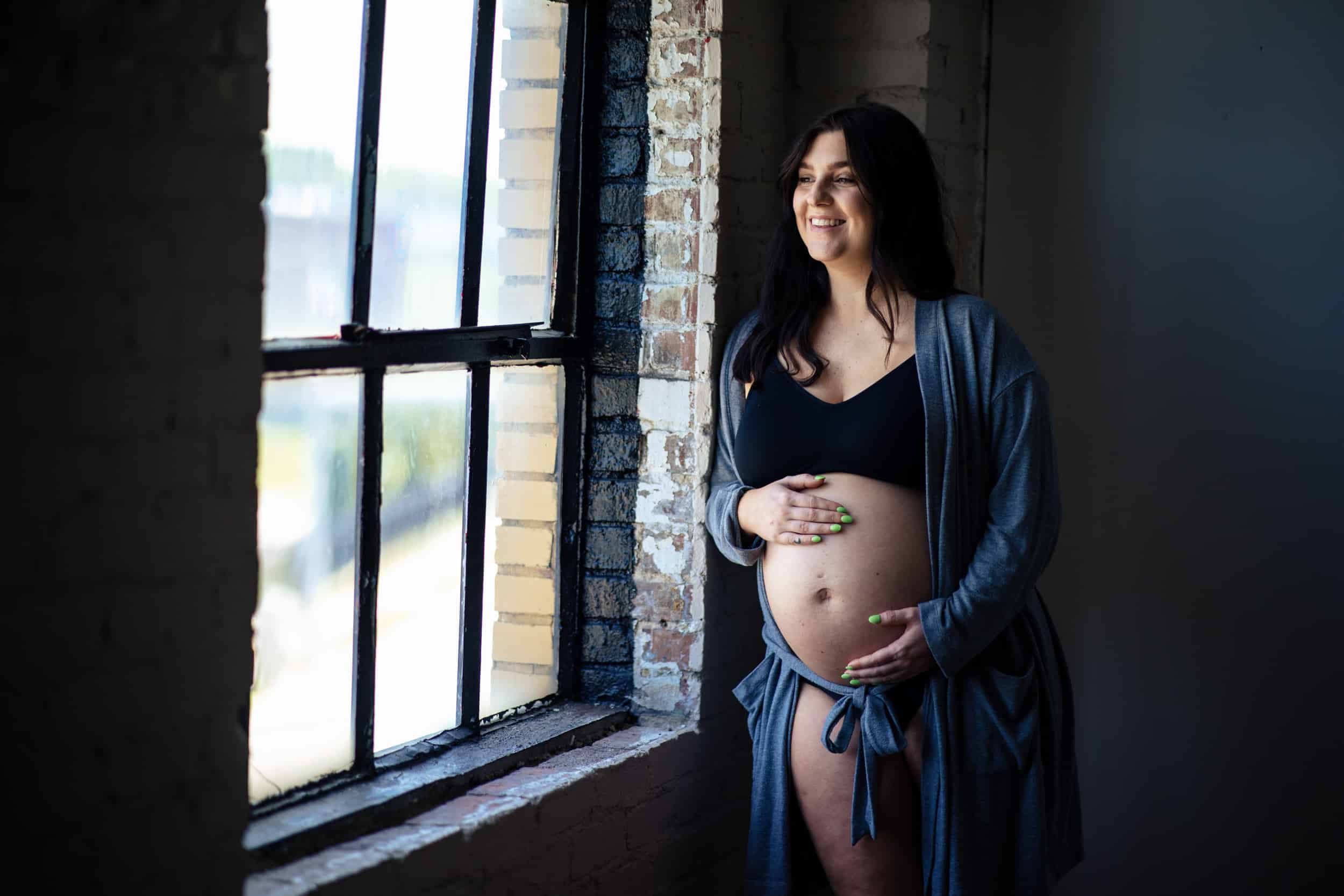 A pregnant woman leaning against a window.