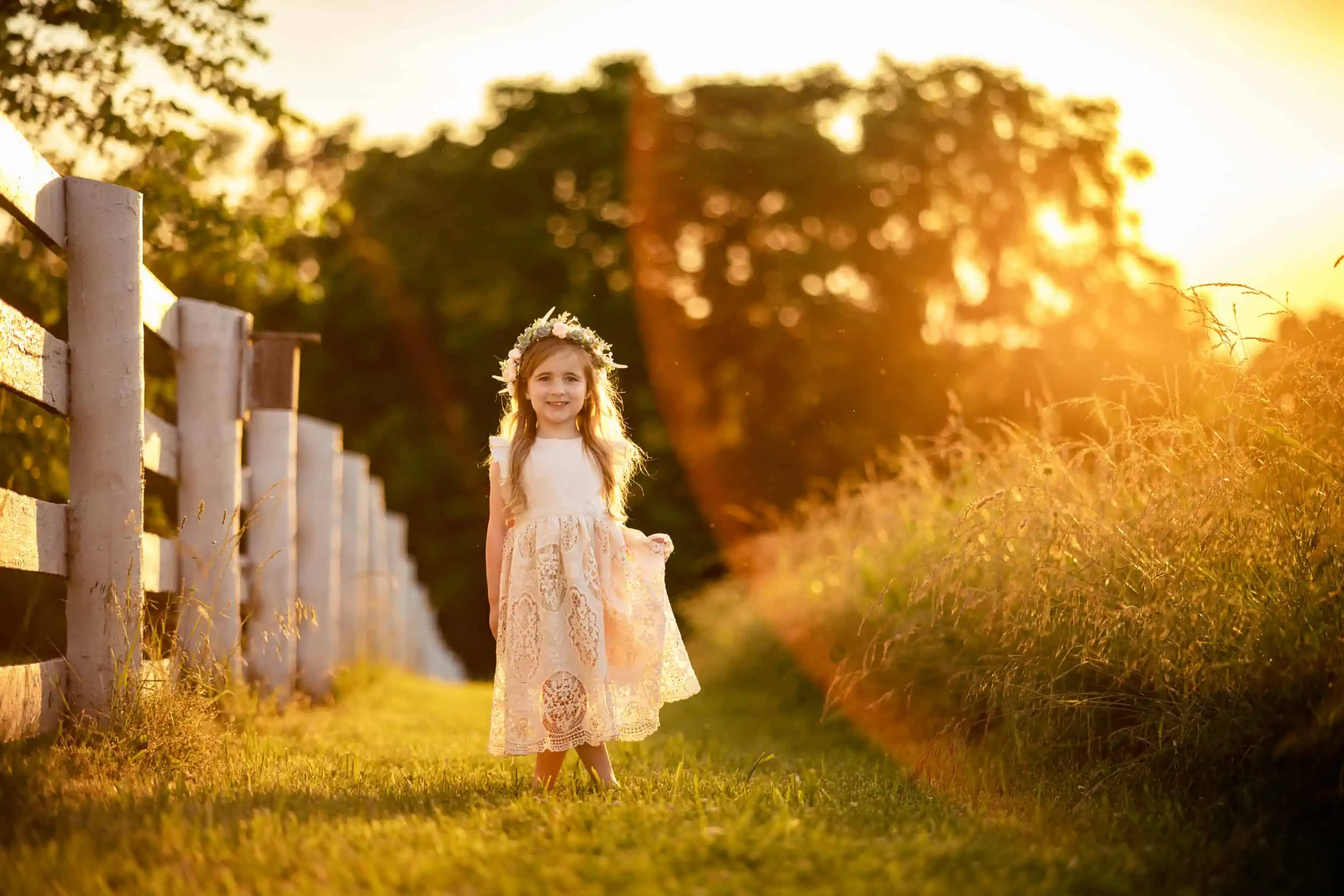 A little girl in a dress walking through a field at sunset.