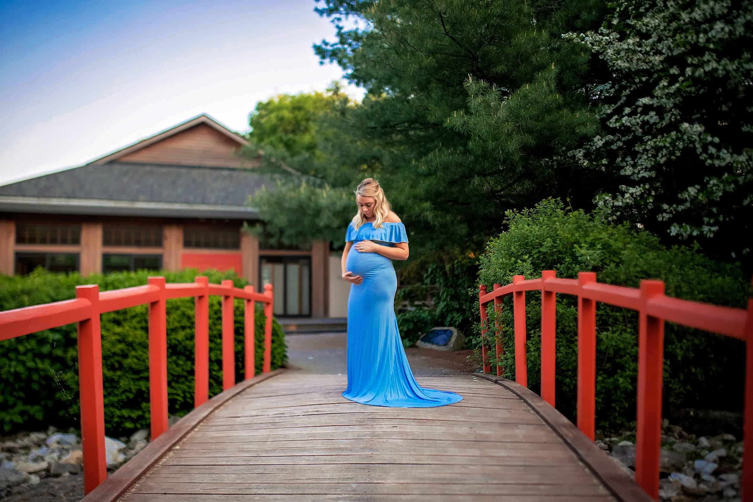 A pregnant woman in a blue dress standing on a bridge.