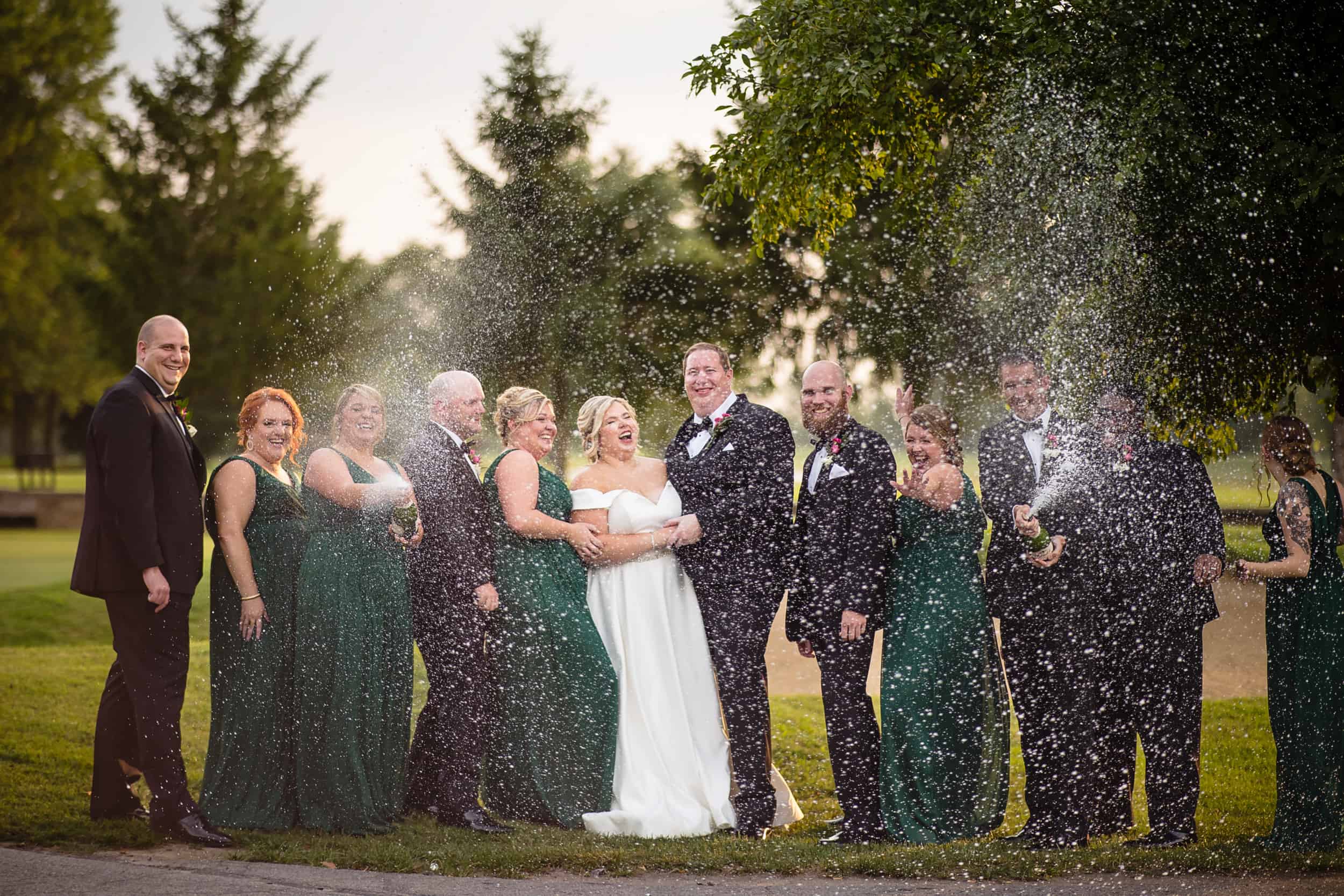 A group of bridesmaids and groomsmen having a water fight at Woodhaven Country Club.