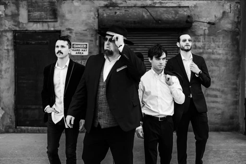 A black and white photo of a group of men in suits and hats by Riptide Productions.