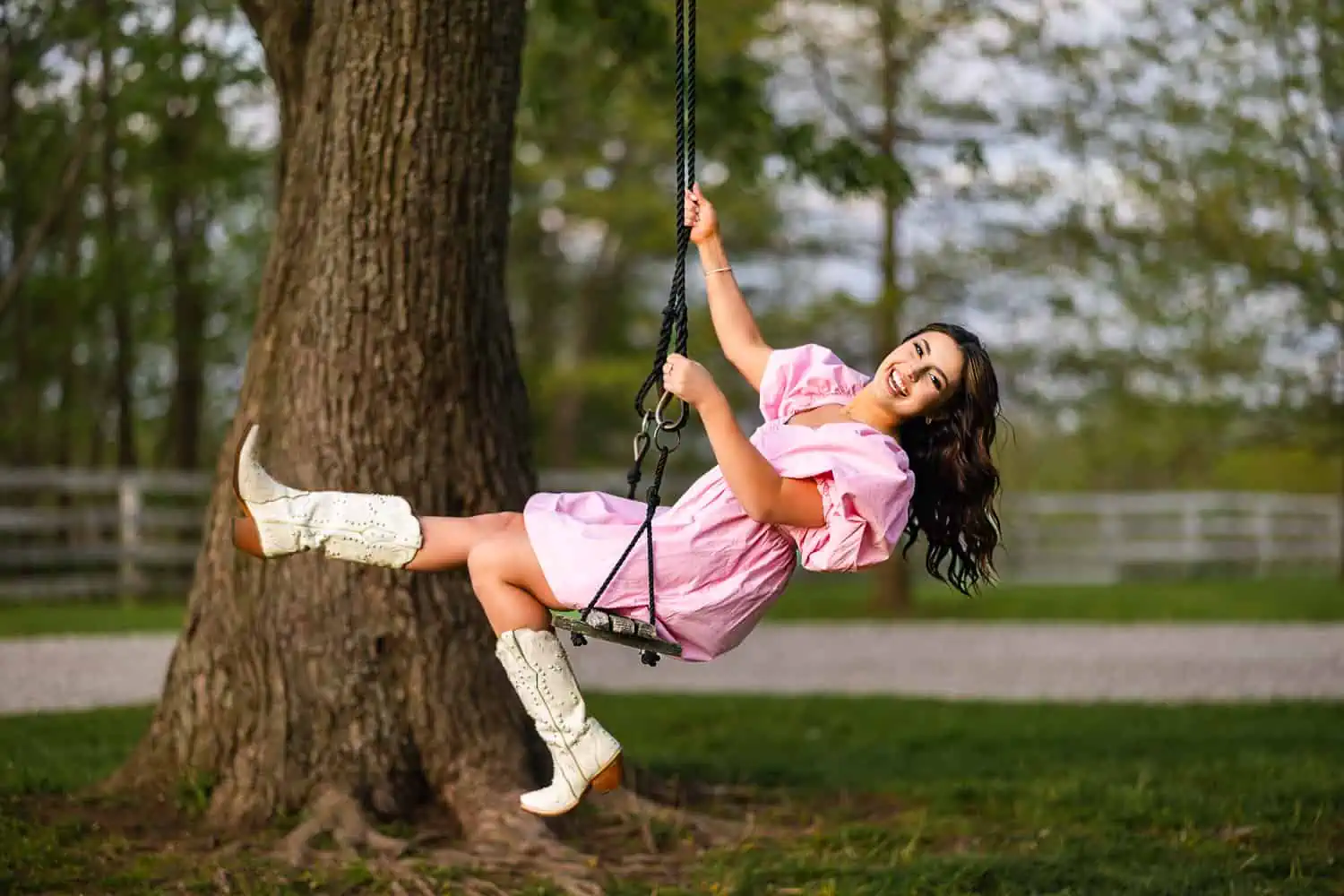 A Lexington senior photographer captures a girl in a pink dress swinging on a tree.