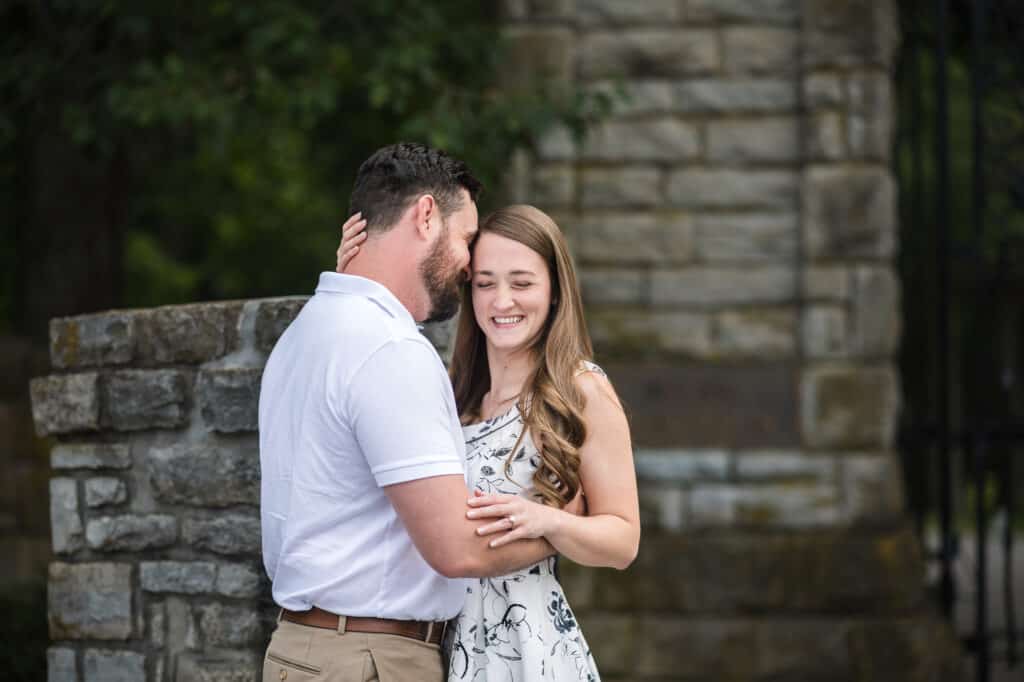 An engaged couple embracing in front of a stone gate for their Frankfort KY engagement photos.