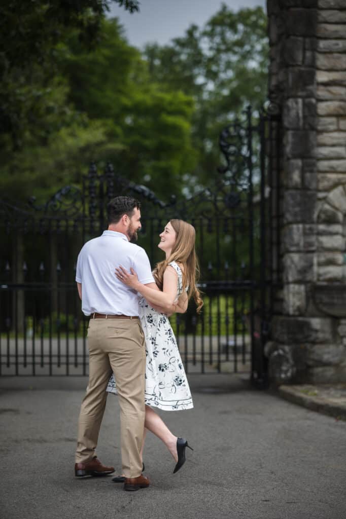 A couple is dancing in front of a stone gate during their Frankfort KY engagement photoshoot.