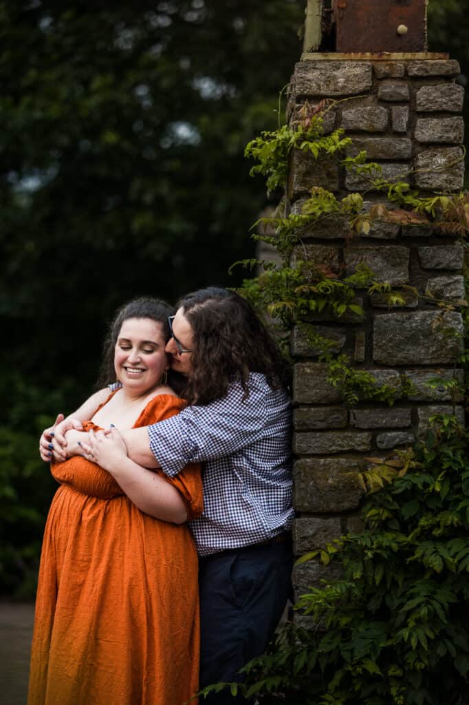 A couple hugging in front of a stone wall during their engagement session at UK Arboretum.
