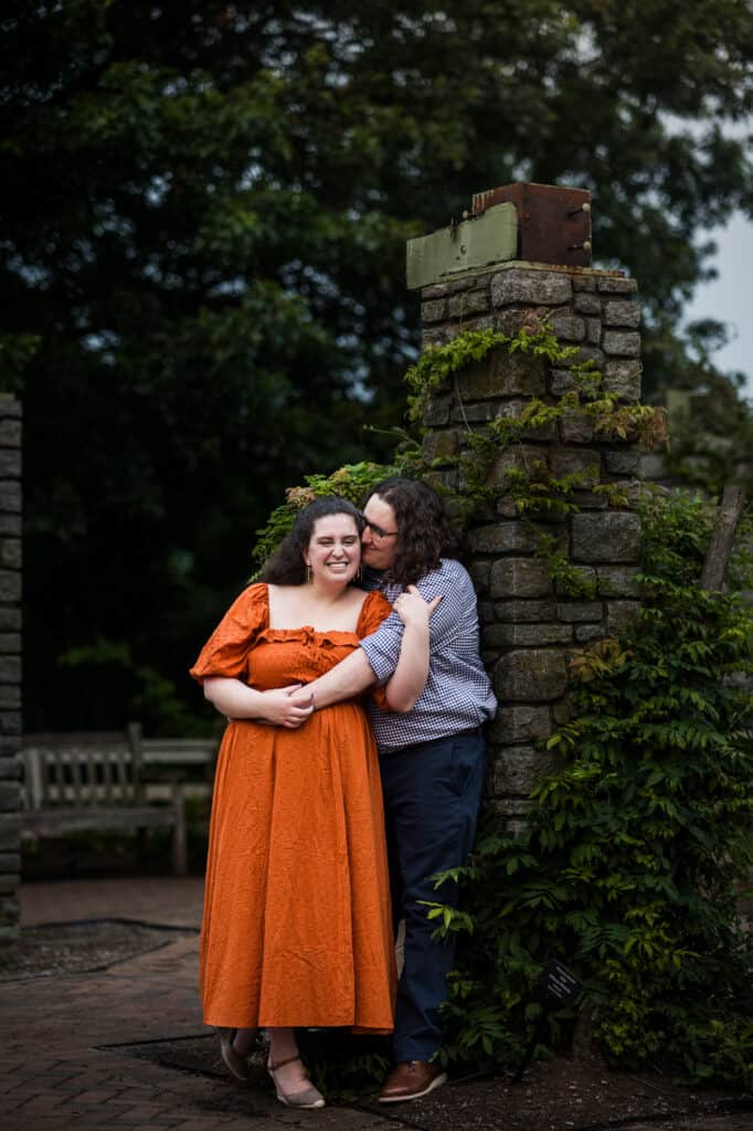 A couple embracing during their engagement session at UK Arboretum, with a stone wall in the backdrop.