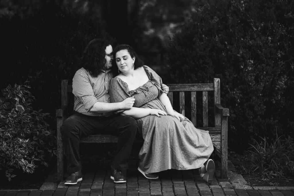 A black and white photo of a couple sitting on a bench during their engagement session at the UK Arboretum.