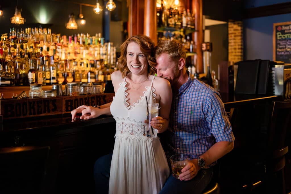 A couple's engagement session at Bourbon on Rye, posing for a photo in front of the bar.
