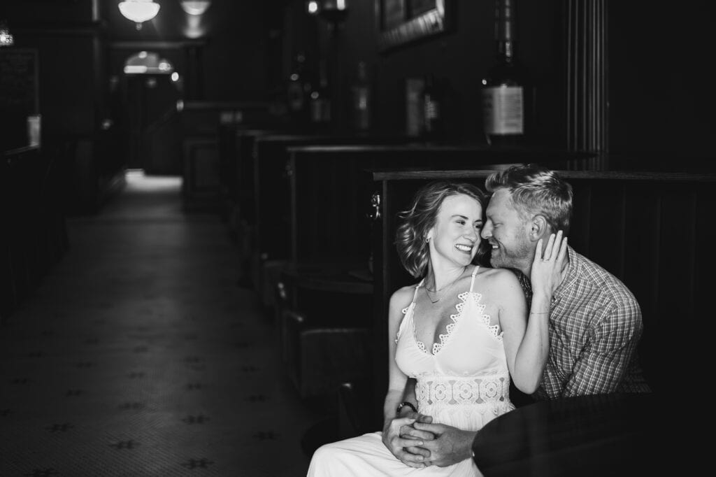 A bride and groom having an engagement session at Bourbon on Rye, sitting on a bench in a dimly lit room.