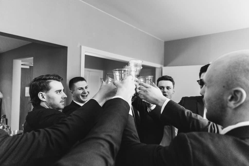 A black and white photo of groomsmen toasting glasses at a Harper Hall wedding.