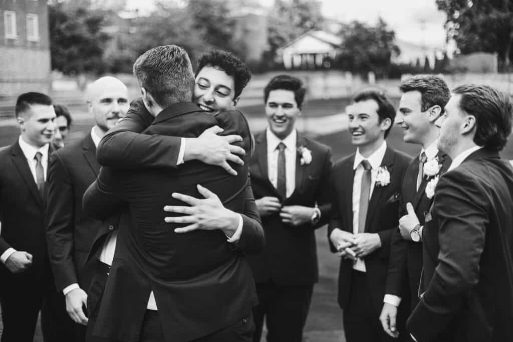 A group of Harper Hall groomsmen hugging each other at a wedding.