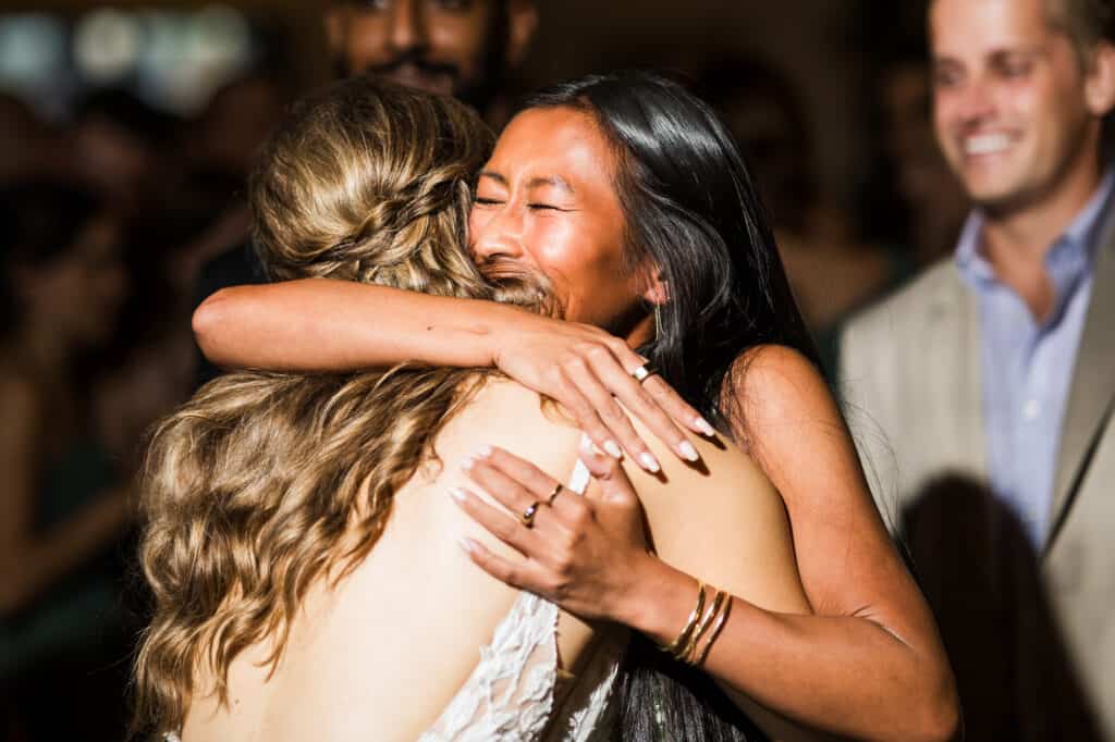 At the Harper Hall Wedding, a bride embraces her bridesmaid during the reception.