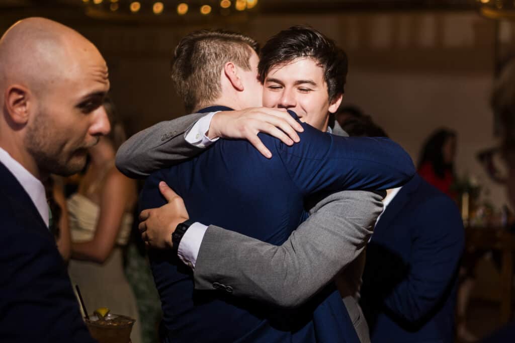 Two men at a Harper Hall wedding reception sharing a warm embrace.