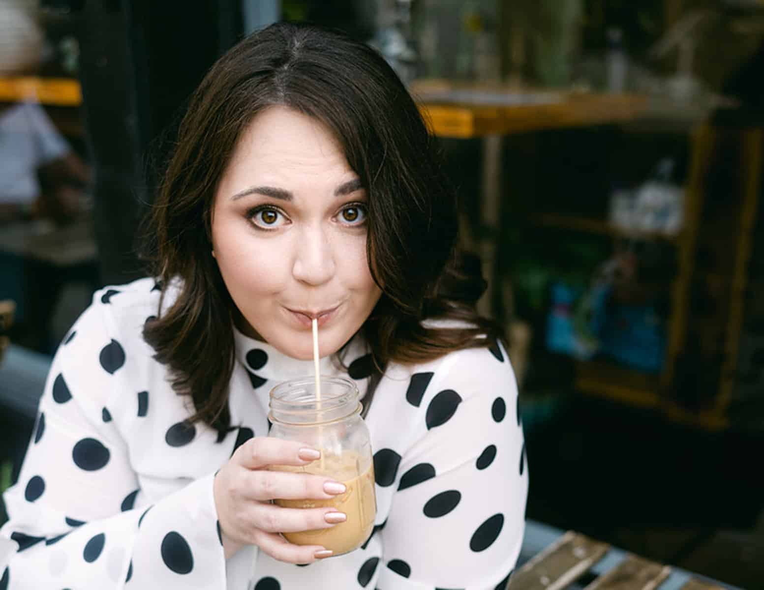 A woman in a polka dot shirt drinking a cup of coffee.