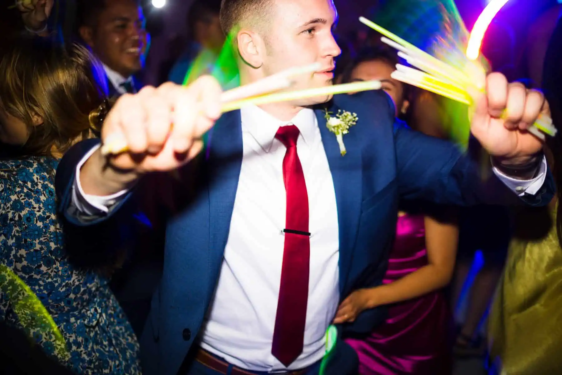 A man in a suit is dancing with a glow stick.