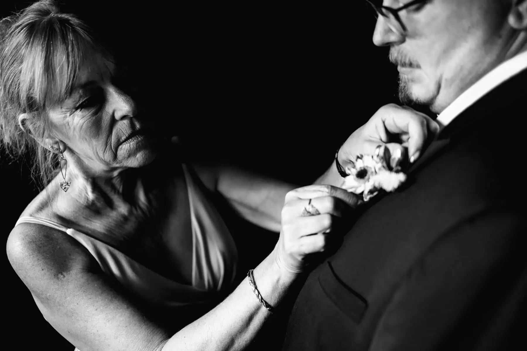 Black and white photo of a woman putting on a man's boutonniere.