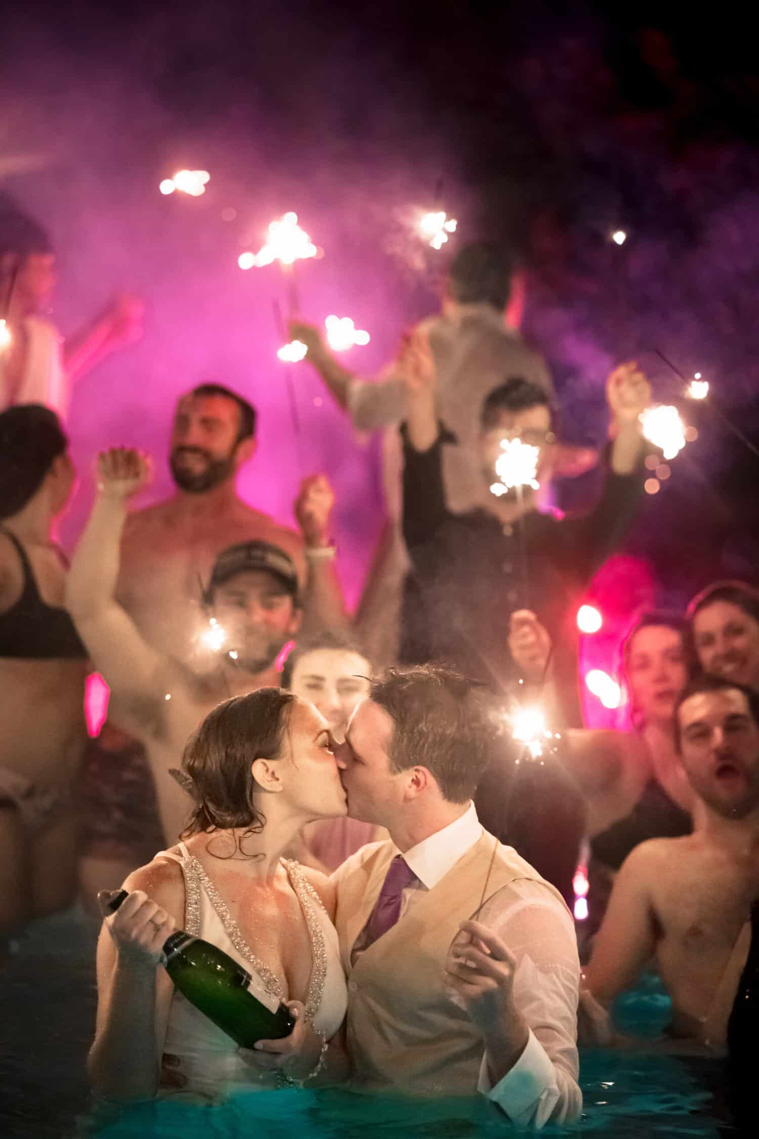 A bride and groom kissing in a pool with sparklers.