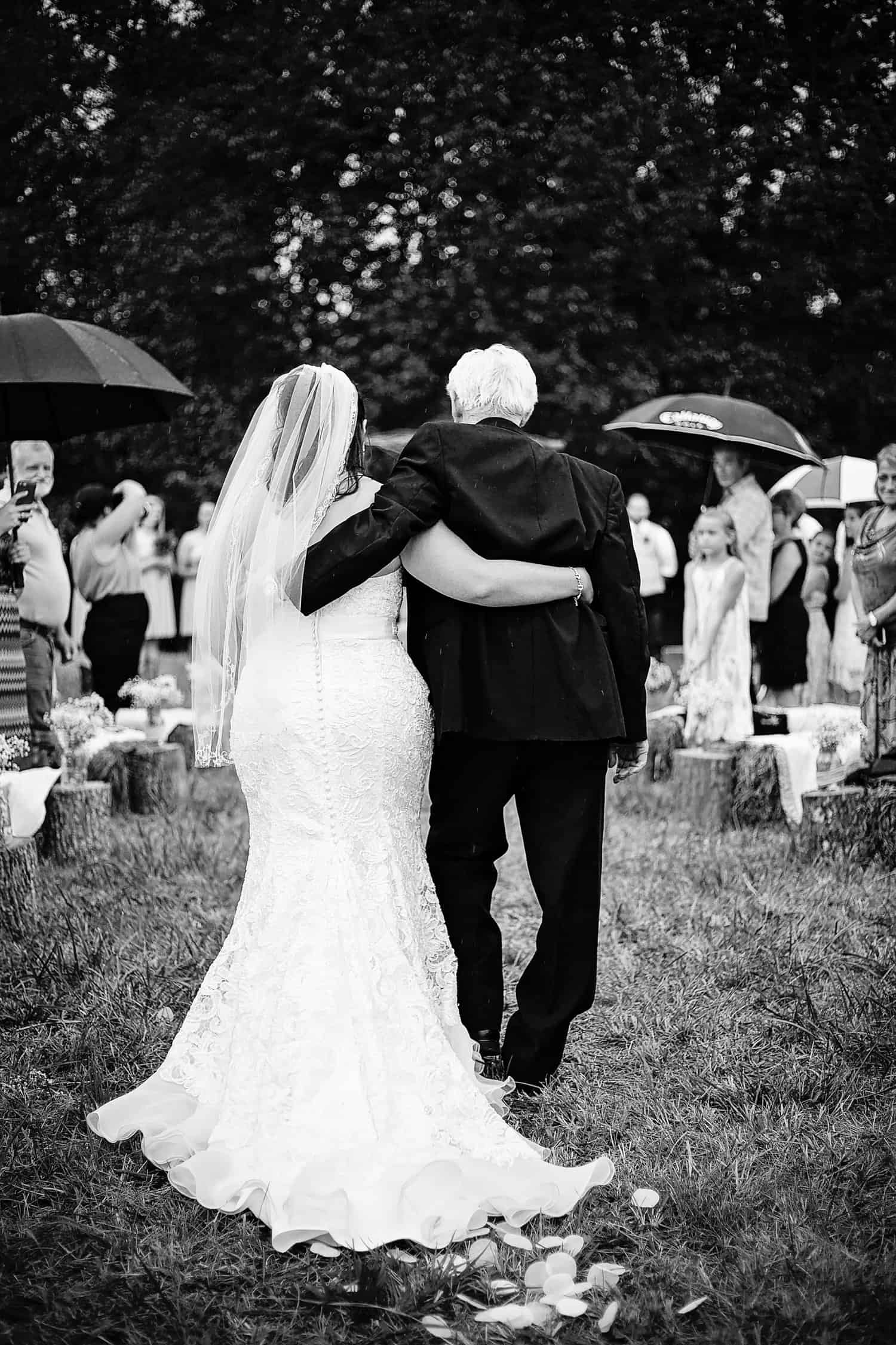 A black and white photo of a bride and her father walking down the aisle.
