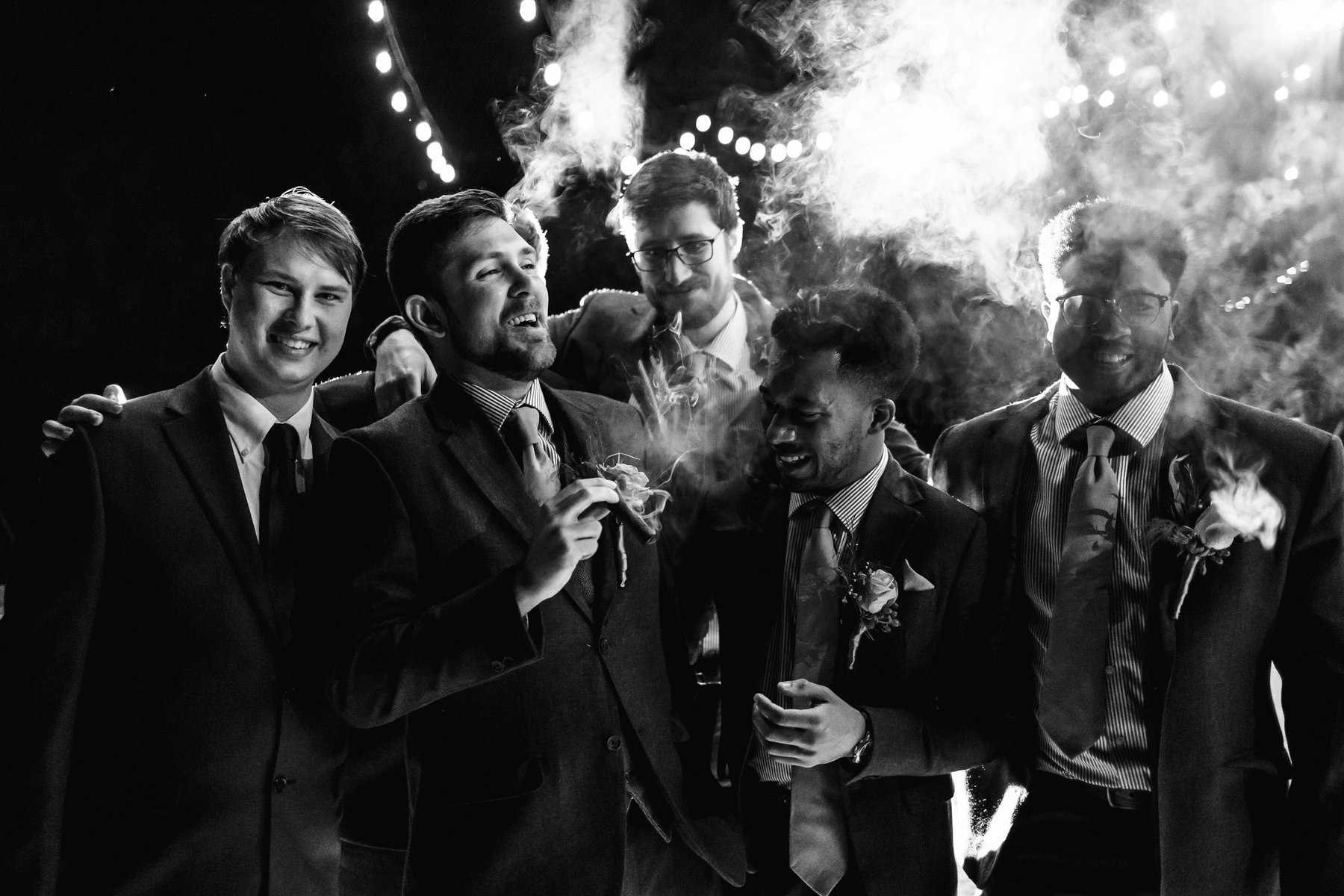 A black and white photo of a group of groomsmen smoking cigars.