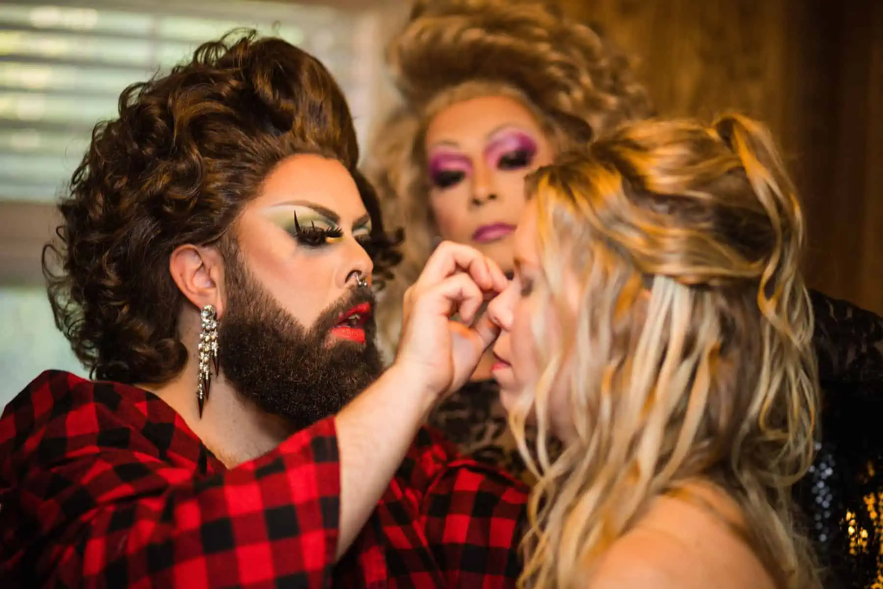 A woman is getting her makeup done by a man with a beard.