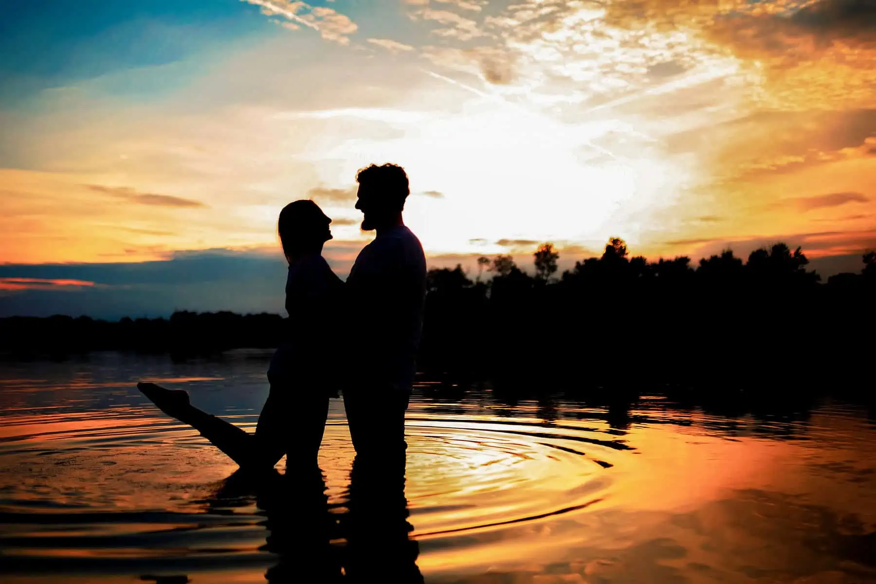A man and woman standing in the water at sunset.