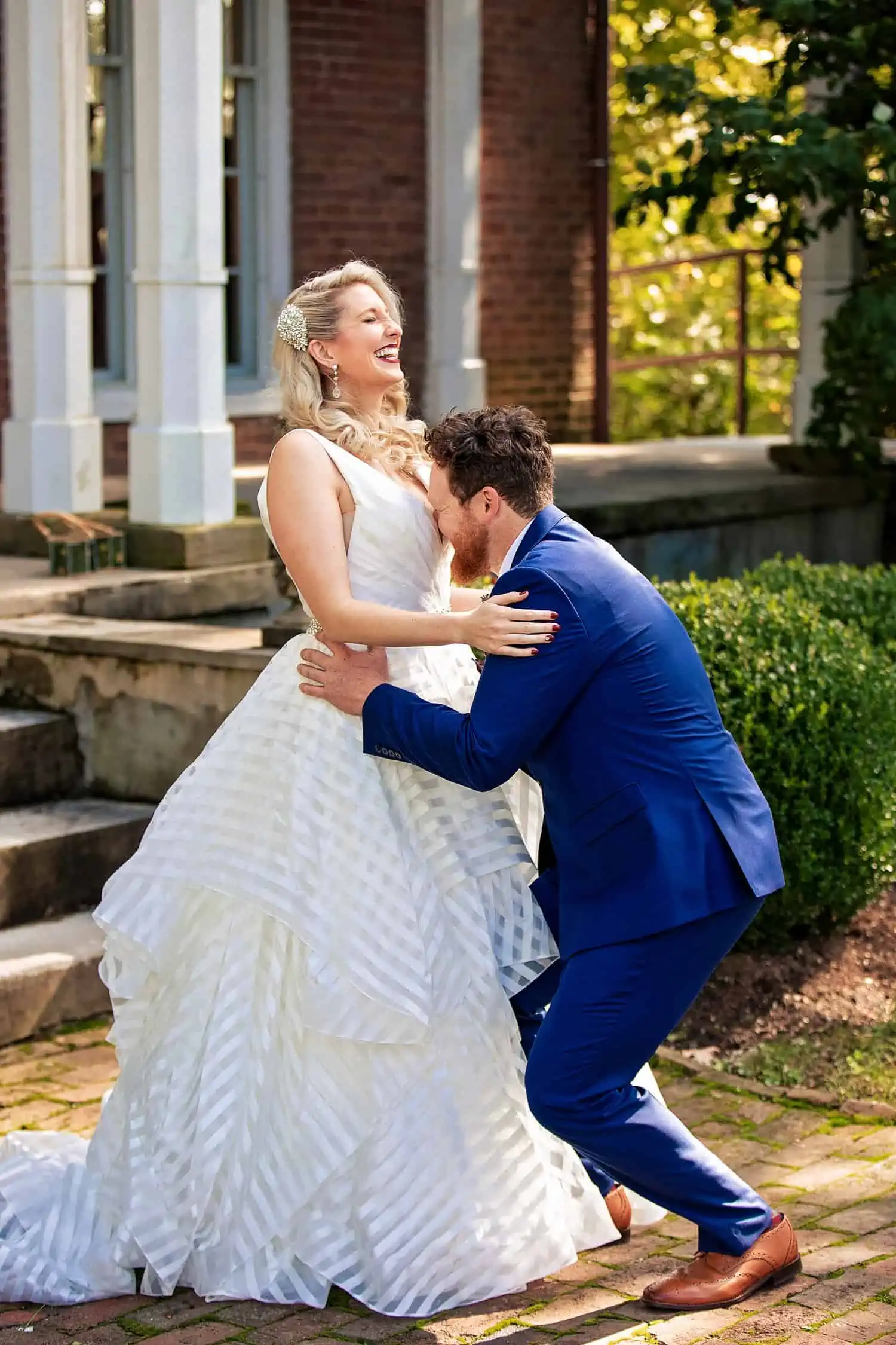 A bride and groom kissing in front of a brick house.