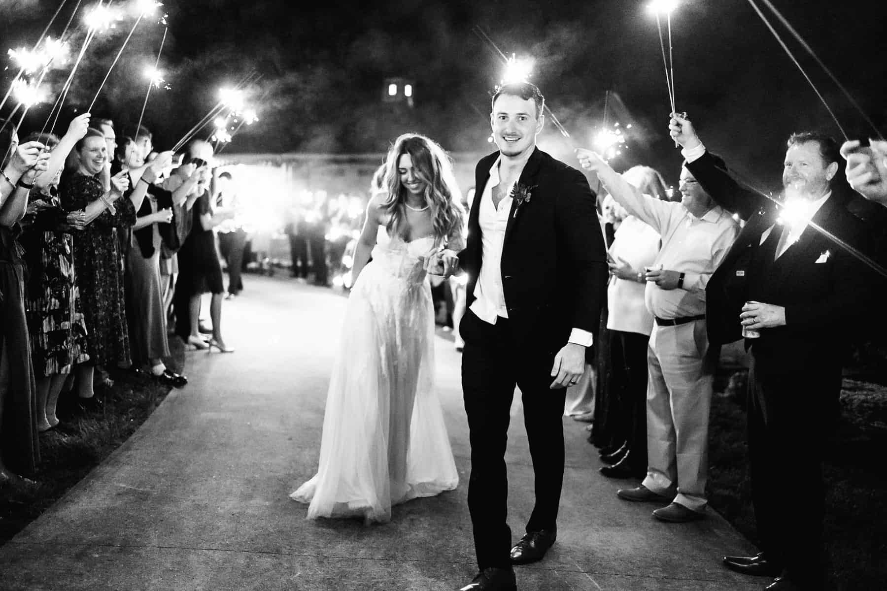 A bride and groom walking down the path with sparklers.