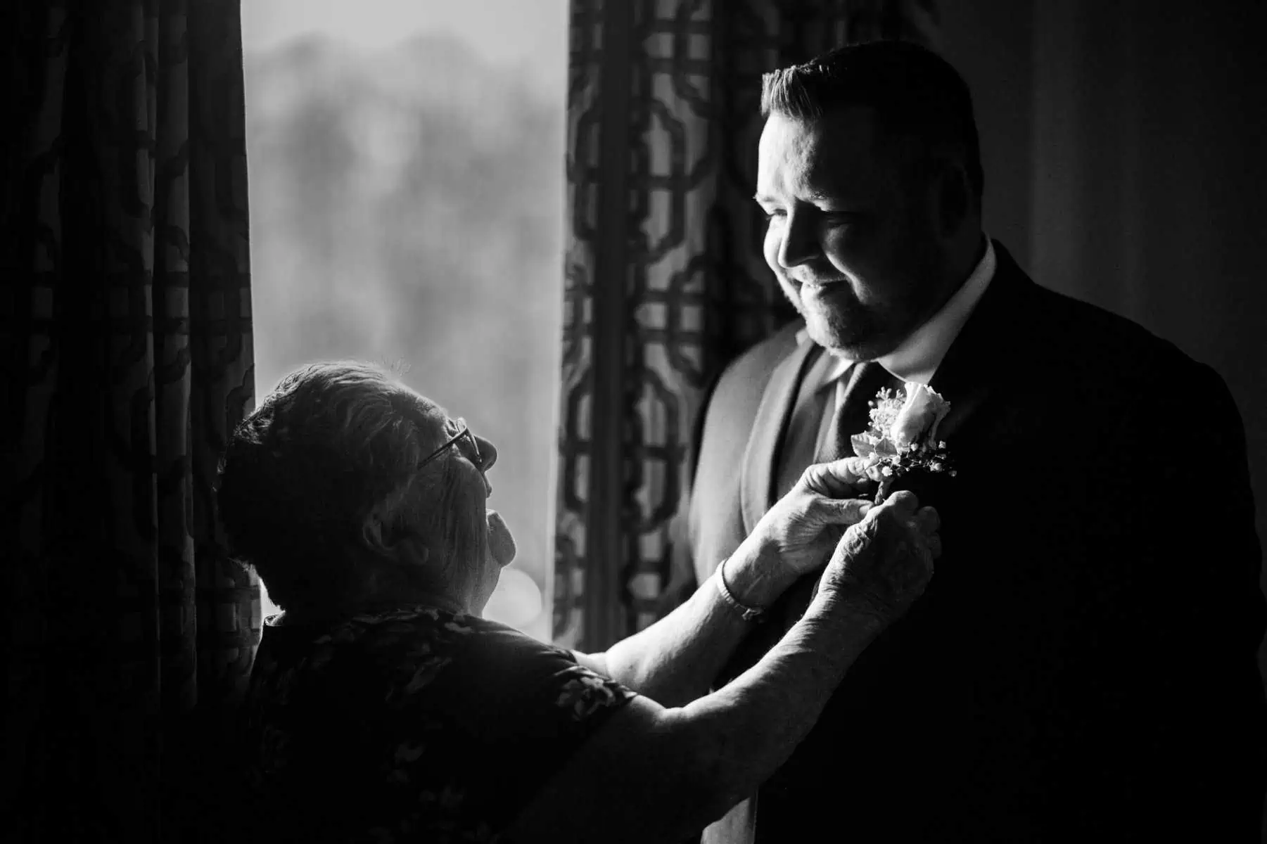 A black and white photo of a man helping his mother with her tie.