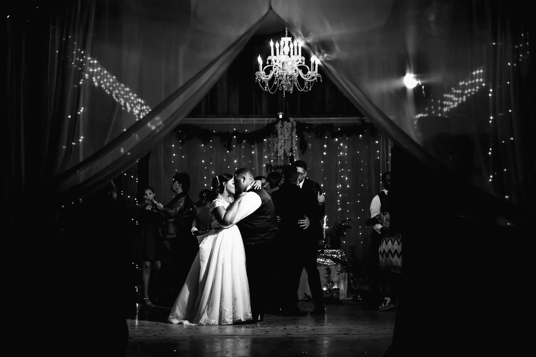 A bride and groom share their first dance in front of a chandelier.