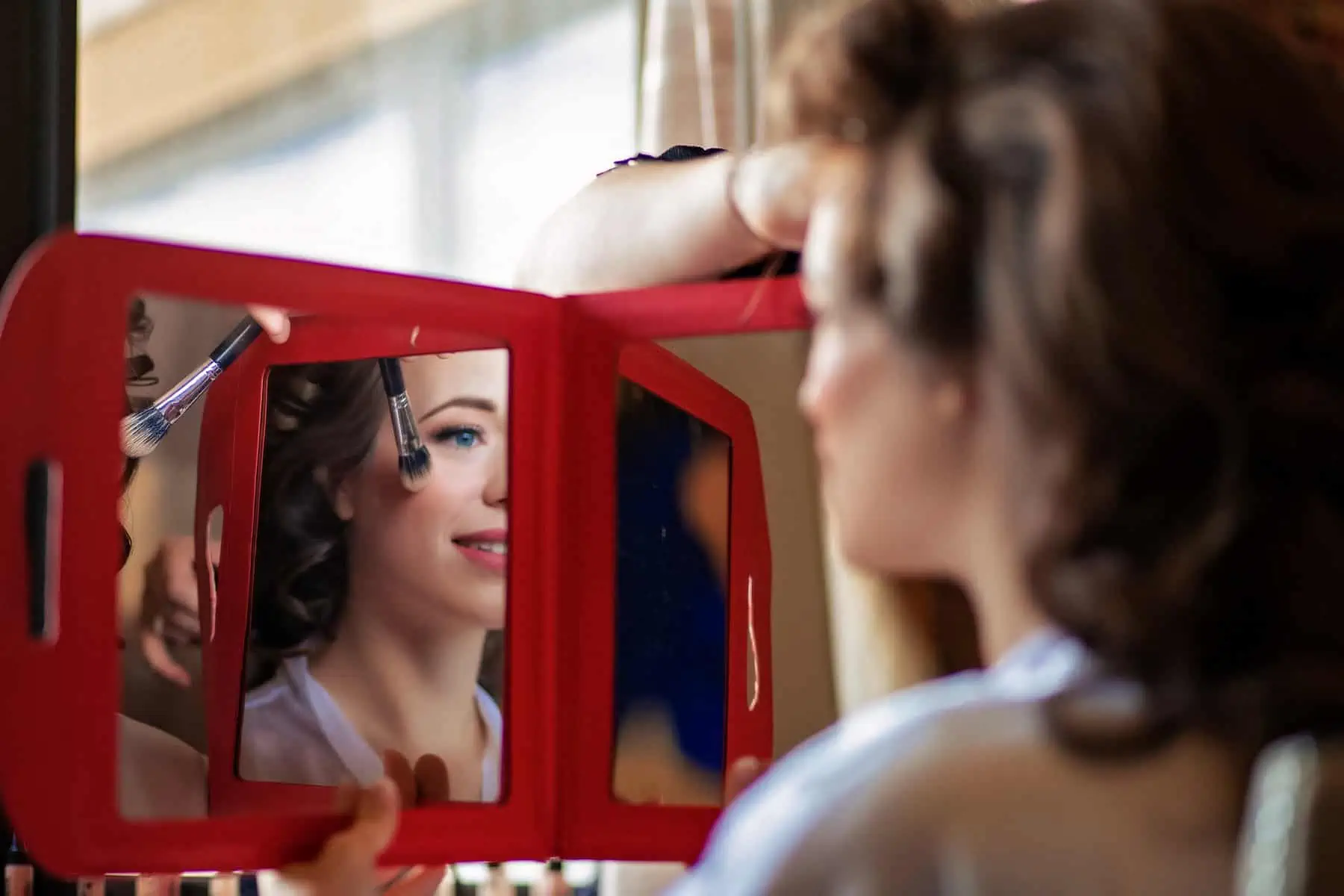 A woman is getting her makeup done in a red mirror.