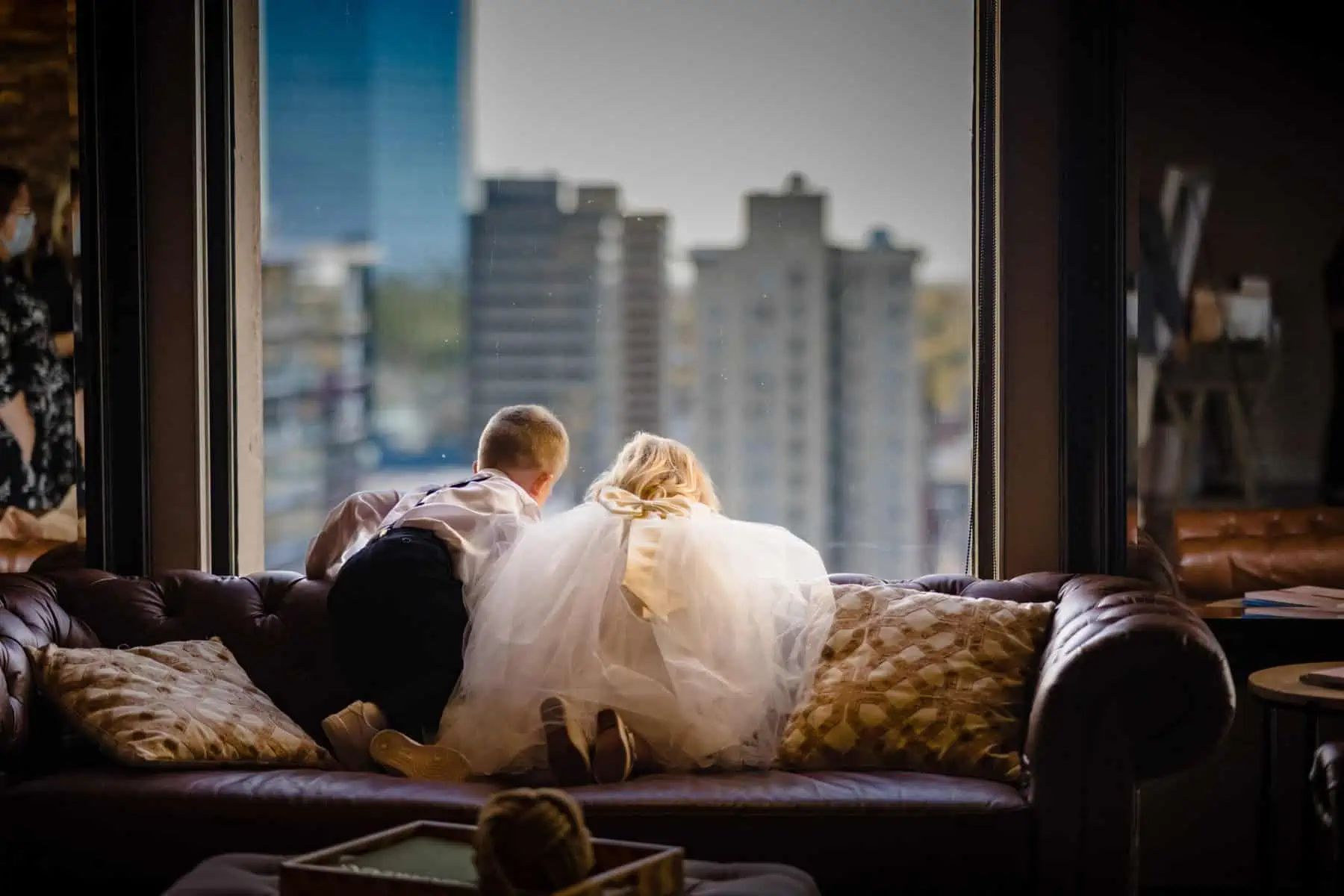 A bride and groom sitting on a couch in front of a window.