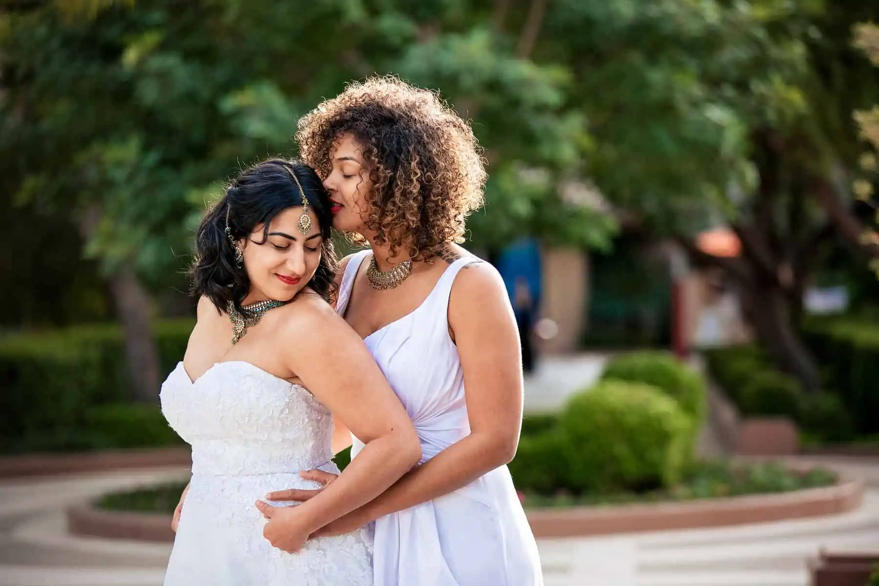 Two brides hugging each other in a garden.