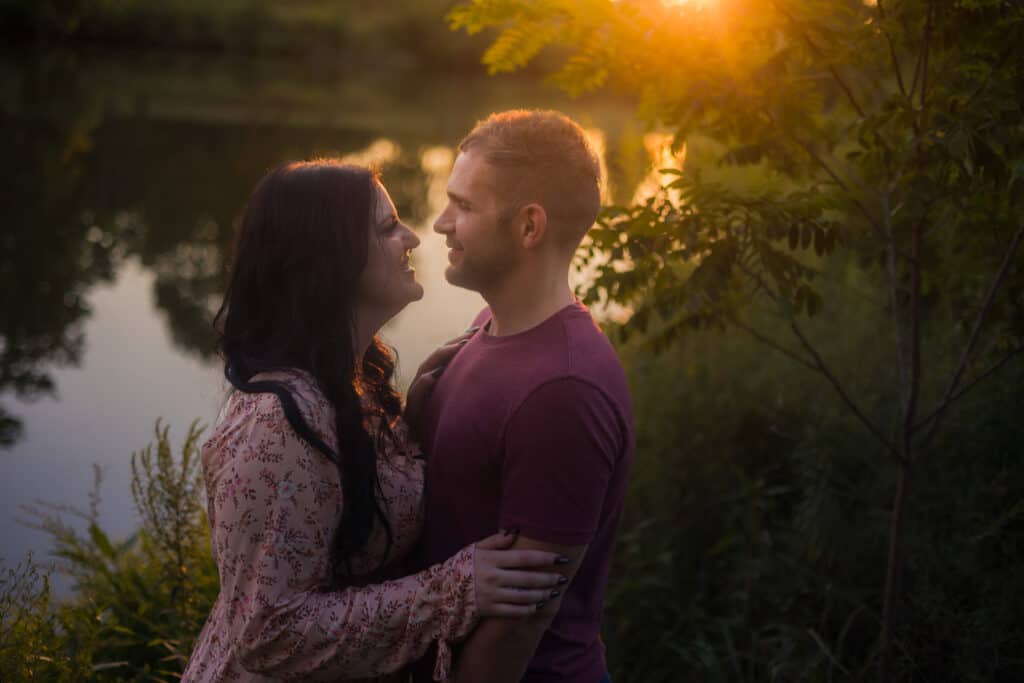  Description: An Engaged Couple Embracing In Front Of A Lake At Sunset During Their Engagement Photoshoot In Harrodsburg.