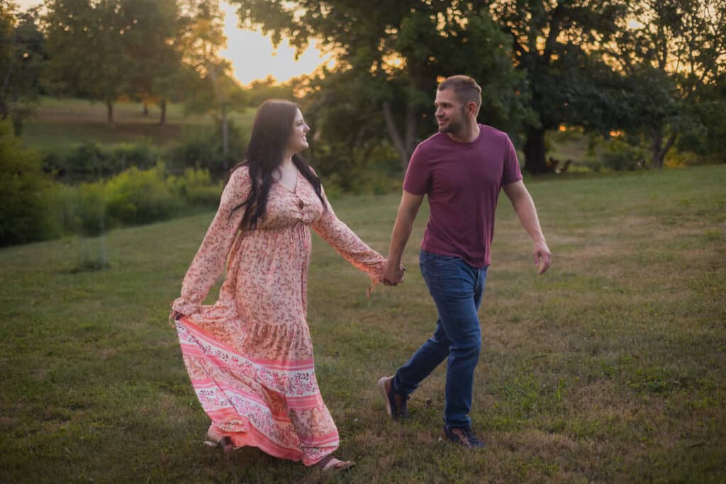A Couple Holding Hands In A Field During An Engagement Photoshoot.