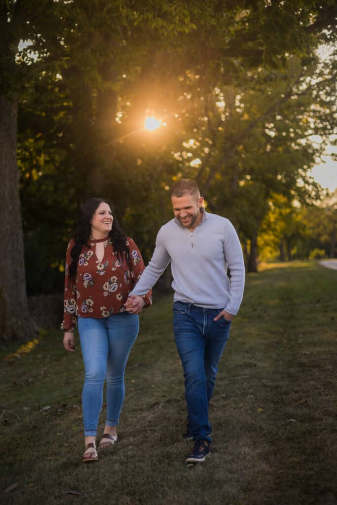 An Engaged Couple Walking Through A Field At Sunset For Their Engagement Photos In Harrodsburg.