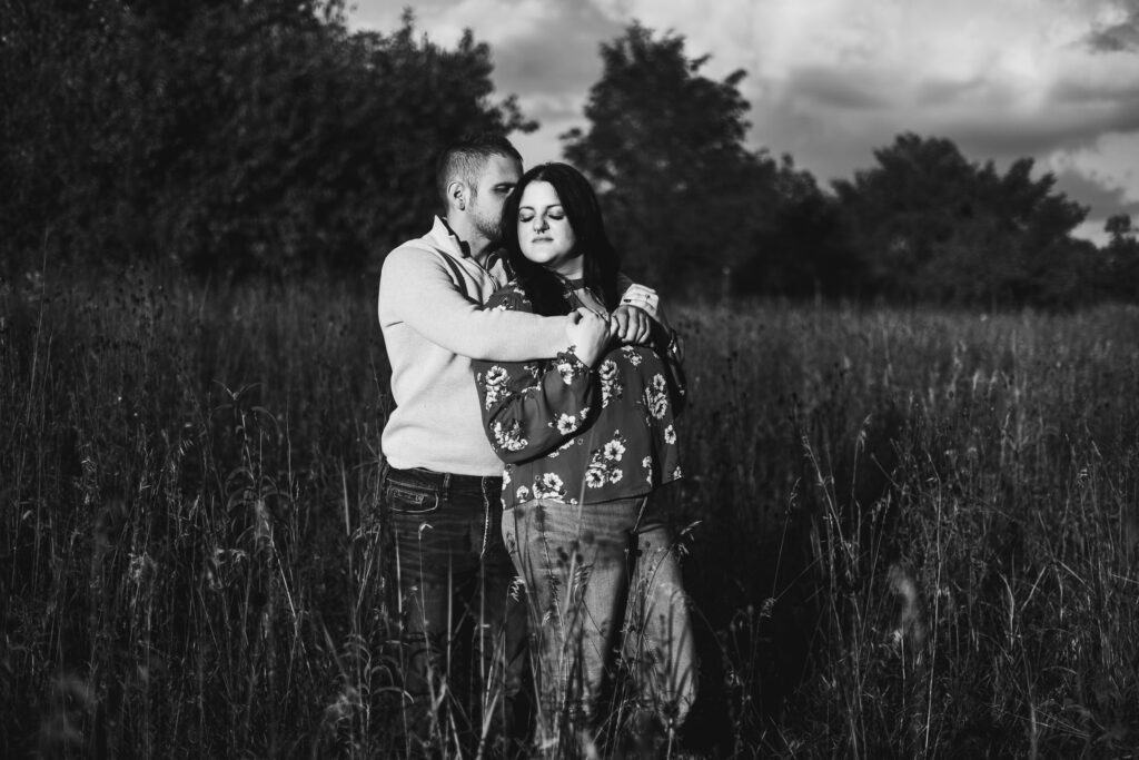 A Black And White Photo Of A Couple Embracing In A Field, Captured During Engagement Photos.