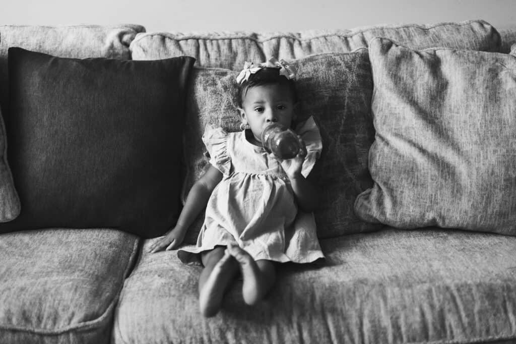 A black and white photo of a little girl sitting on a couch during newborn twin photography in Lexington.