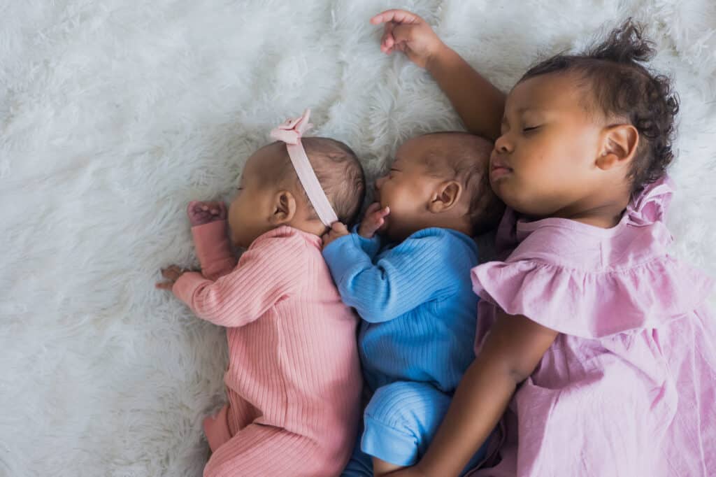 Three newborn babies peacefully sleeping on a white blanket during a twin photography session in Lexington.