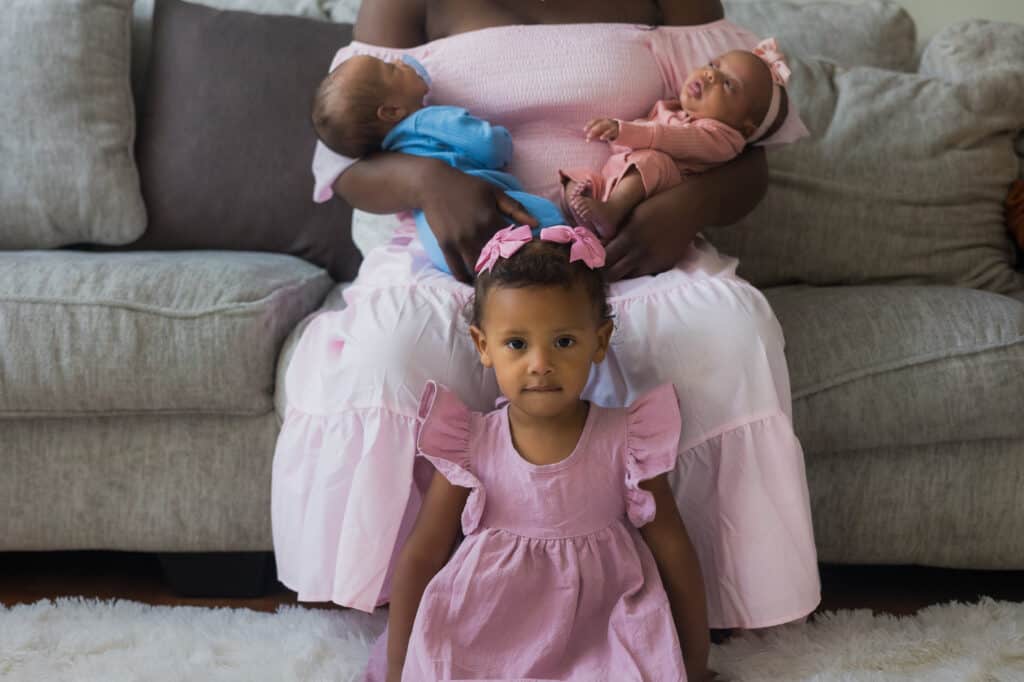 A woman in a pink dress sitting on a couch with her newborn twins for an adorable photography session in Lexington.