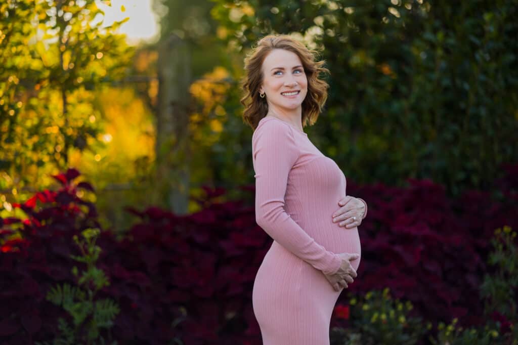 A pregnant woman in a pink dress poses for a photo with a Lexington KY Maternity Photographer.