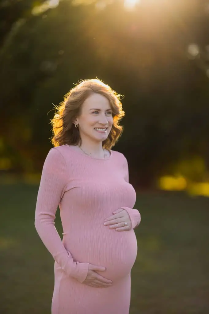 A pregnant woman in a pink dress standing in a park, captured beautifully by a Lexington KY maternity photographer.