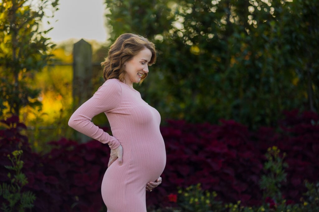 A pregnant woman in a pink dress standing in a field, captured by a Lexington KY Maternity Photographer.