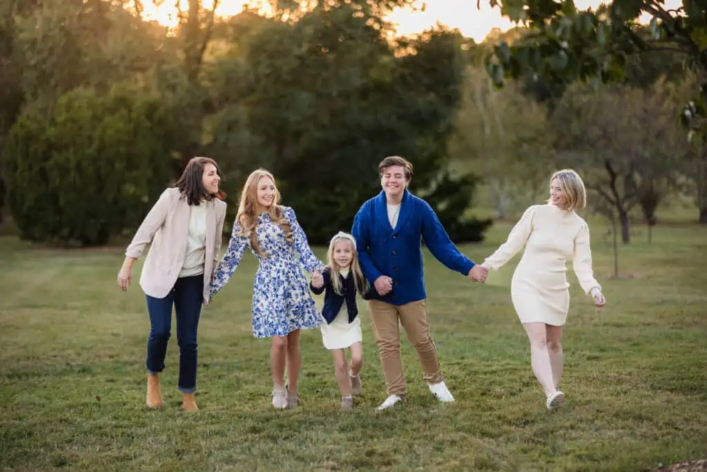 A LGBTQ+ family holding hands in a grassy field at sunset, captured by a photographer in Lexington, Ky.