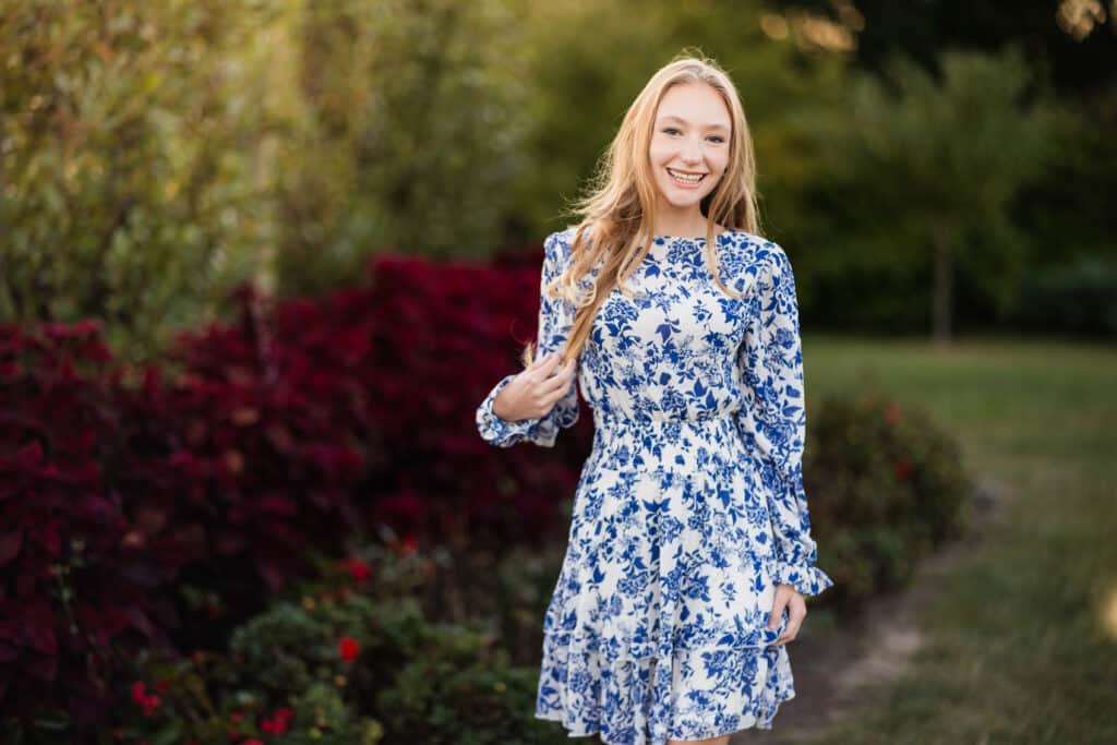 A blonde woman in a blue floral dress smiling in a park, captured by an LGBTQ+ family photographer in Lexington.