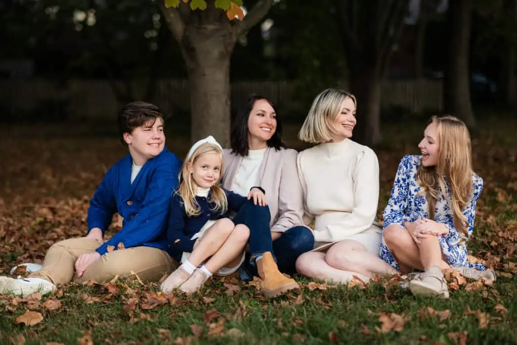 An LGBTQ+ family sits on the ground in front of a tree.