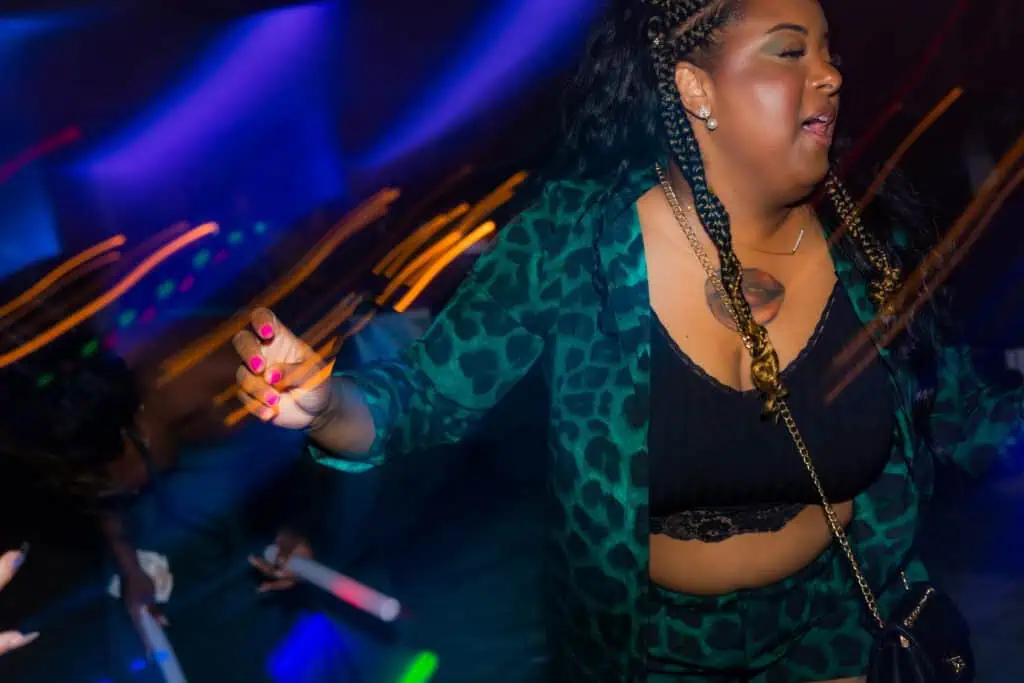 A woman in a leopard print outfit dancing at a nightclub with colorful light streaks in the background.