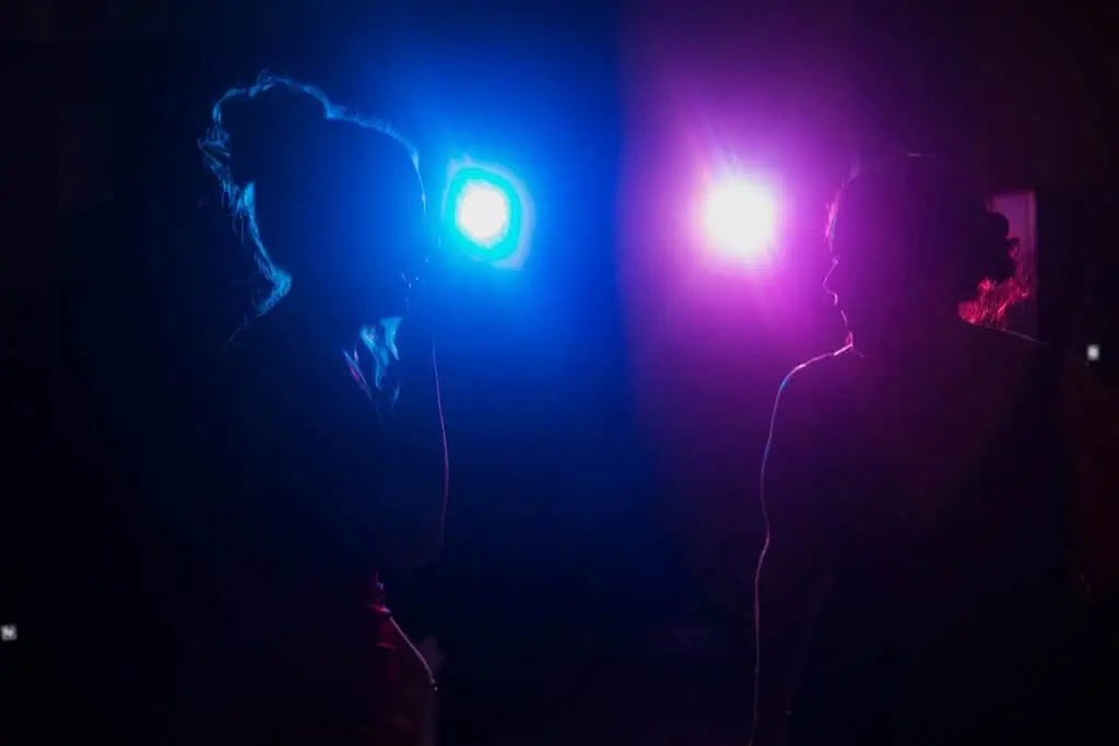 Two women in silhouette converse under dramatic backlighting at a dimly lit event.